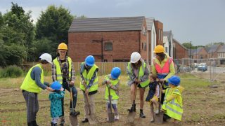 group of people standing on a site digging in hard hats